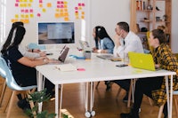 a group of people sitting around a table with laptops