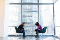 two women sitting in chairs in front of a large window